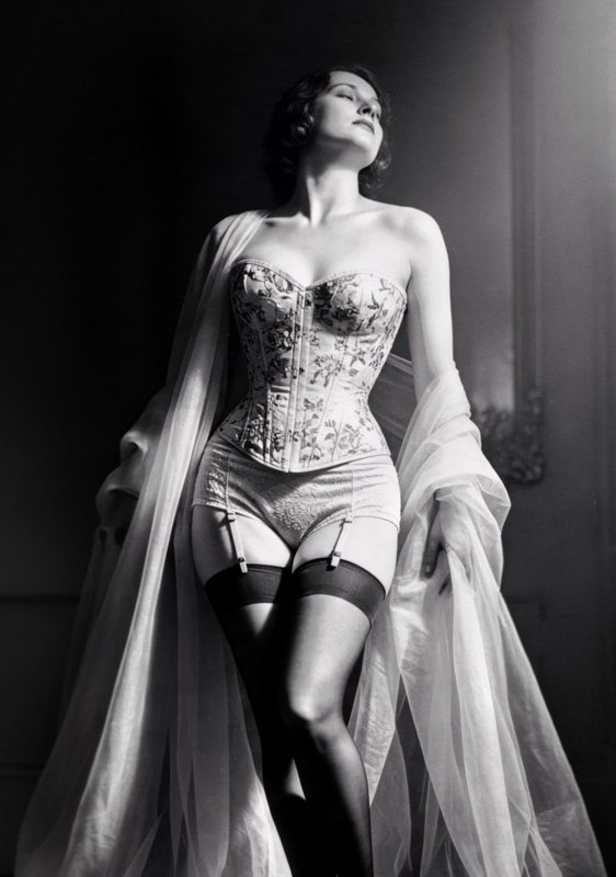 Vintage-style woman in floral corset with stockings and sheer cape in black-and-white.