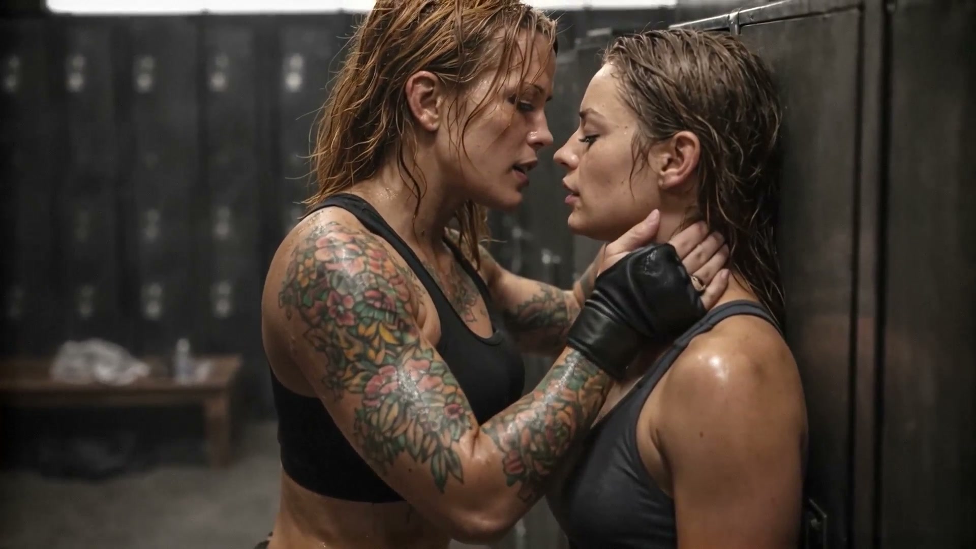 Two tattooed women in a gym locker room face off, one holds the other's neck in a tense moment.