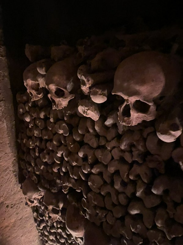 Stacked human skulls and skeletal bones line a decorative ossuary wall in the dimly lit undergrou...
