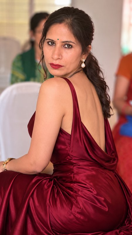 Elegant South Asian woman in a deep burgundy satin gown looks over her shoulder at a formal indoo...