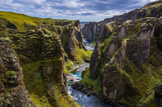 Winding turquoise glacial river flows through moss-covered jagged canyon walls in remote Iceland