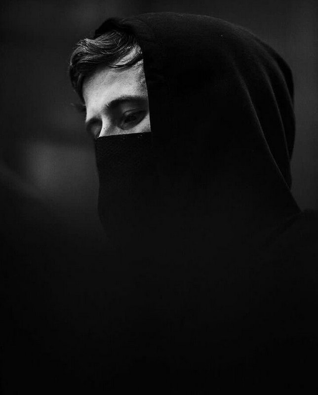 Monochrome close-up portrait of a hooded person, most of their face covered, only their eyes and ...