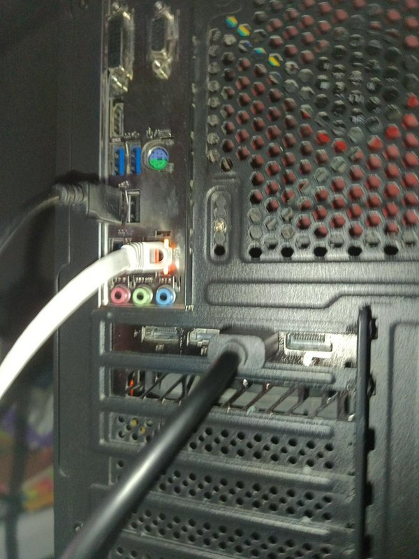 Close up of rear desktop PC I/O panel with connected cables, motherboard ports, and vented case