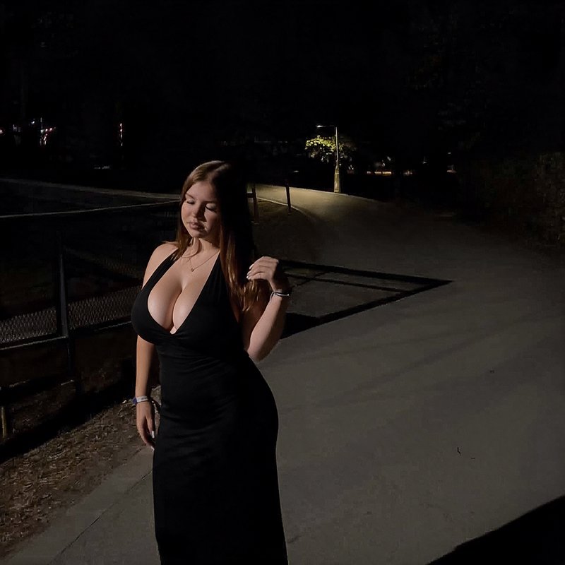 Young woman in a form-fitting black gown poses on a lit sidewalk at night