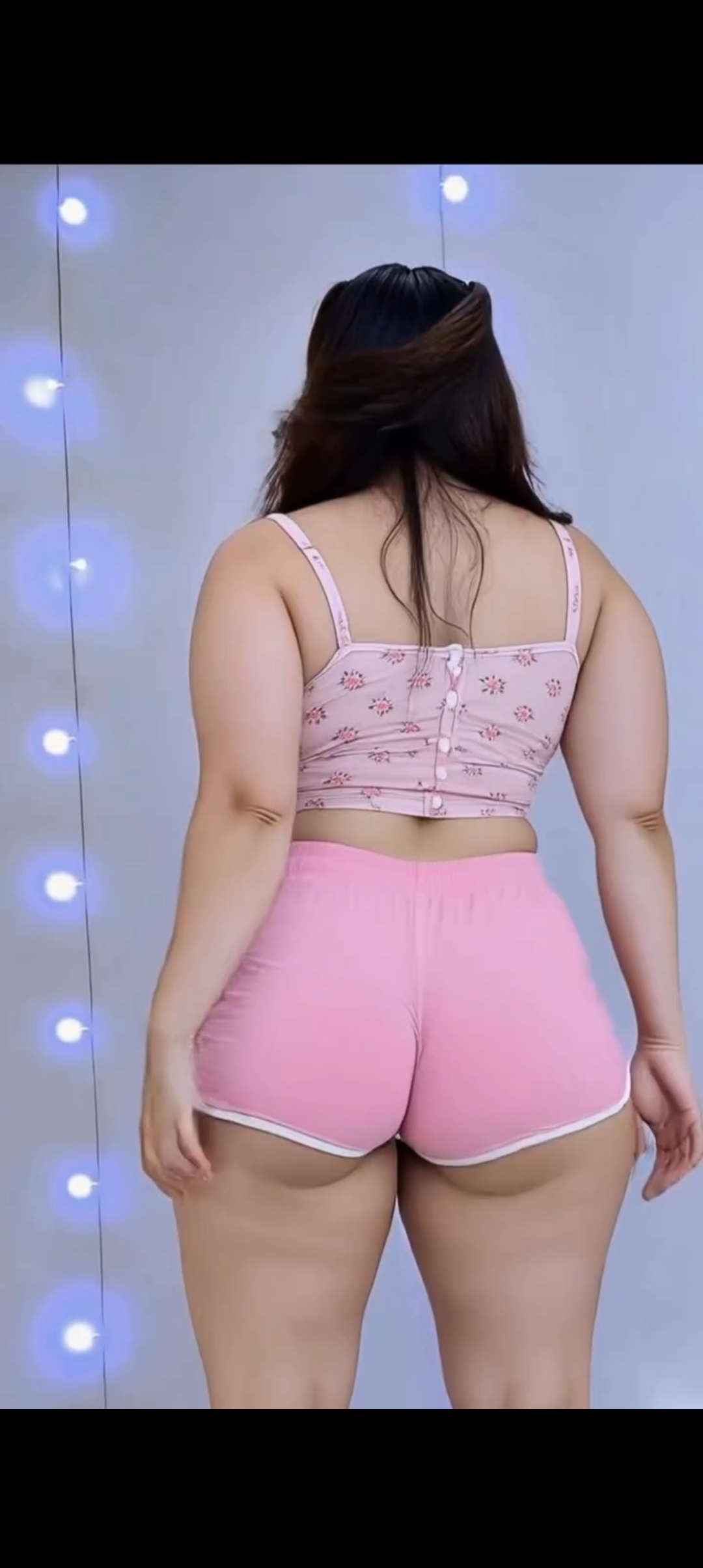 Back view of a woman in a matching pink loungewear set standing in front of a lit indoor wall
