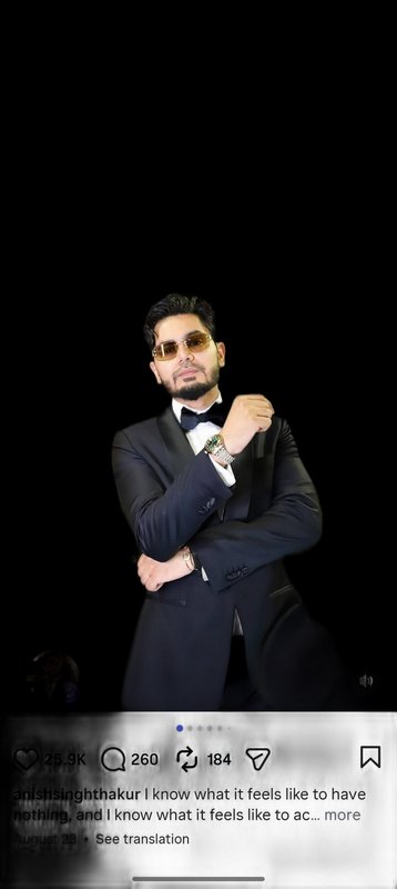 Confident man in a black formal tuxedo and sunglasses poses against a black backdrop in a social ...