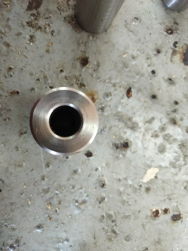Top-down view of a machined hollow metal pipe flange resting on a worn workshop concrete floor