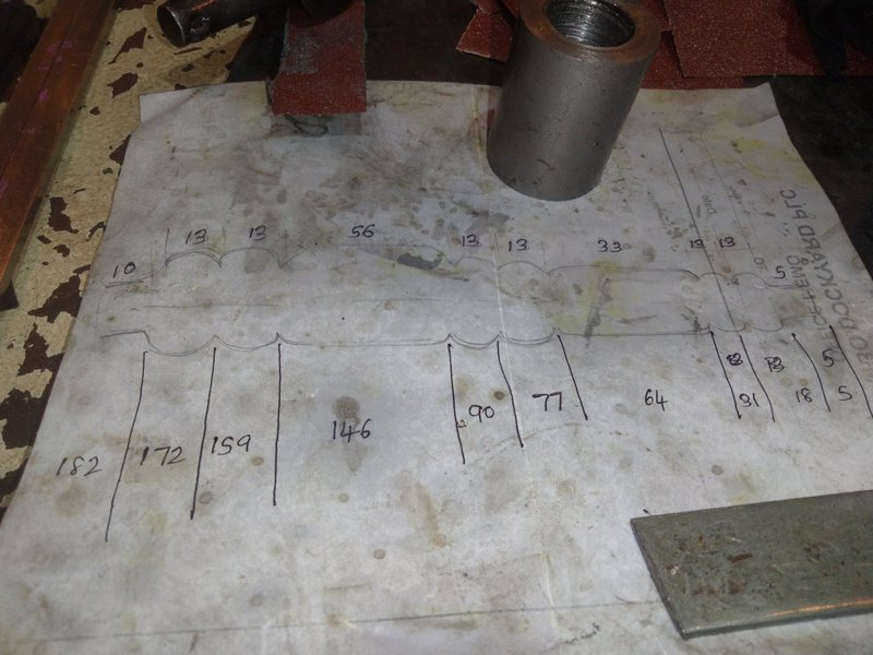 Hand-drawn dimensional layout sketch rests on a worn workbench next to metal workshop components