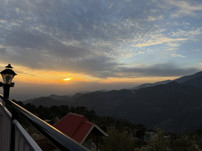 Golden hour sunset over layered forested mountain ranges viewed from a hilltop balcony