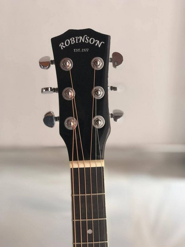 Close up of a Robinson acoustic guitar headstock with tuning pegs and strings against a plain neu...