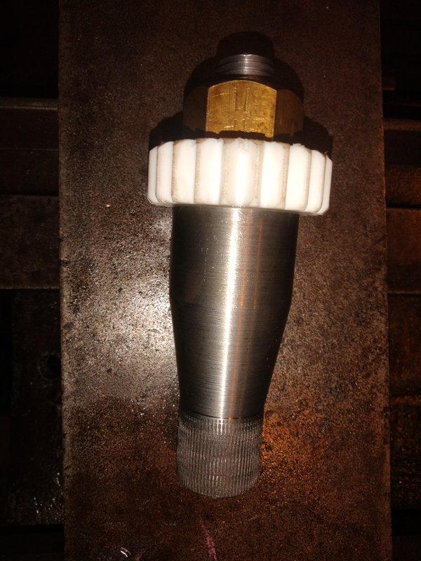 Custom machined industrial fitting with brass nut and plastic collar resting on a workshop workbench