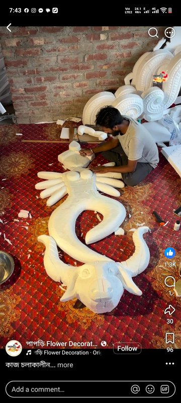 Craftsman shaping a large unfinished styrofoam festival sculpture while seated on a patterned wor...