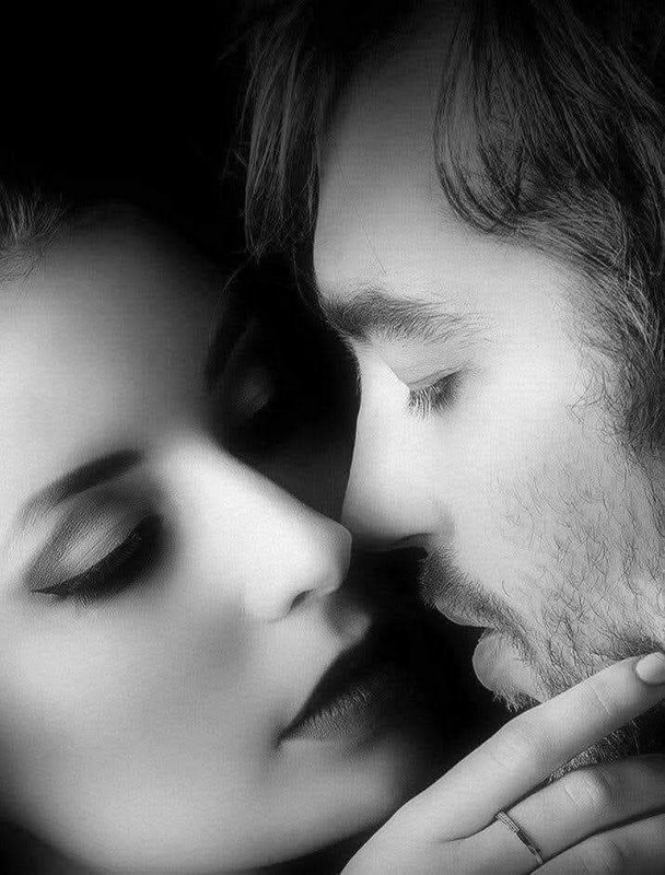 Black and white close-up of an intimate couple leaning in to share a tender kiss, eyes closed.