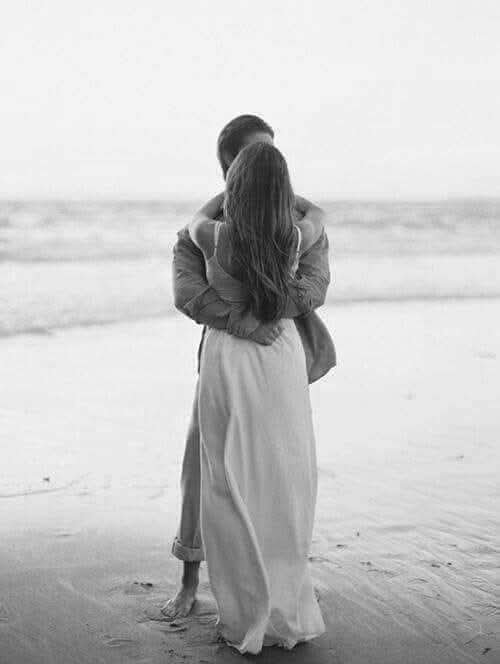 Couple embracing barefoot on a quiet beach facing gentle ocean waves