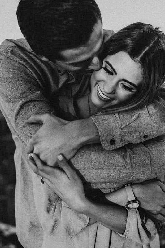 Man embraces a joyful laughing woman from behind in a warm intimate black and white couple portrait