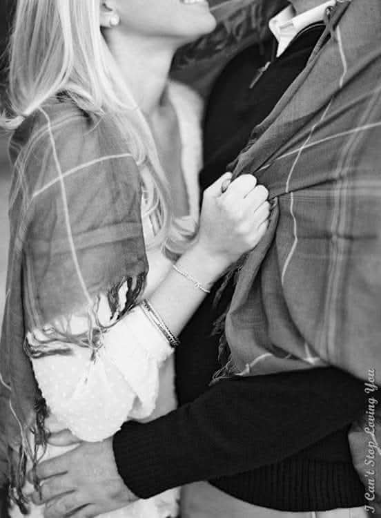 Laughing affectionate couple embracing under a shared plaid blanket in a close cropped black and white shot