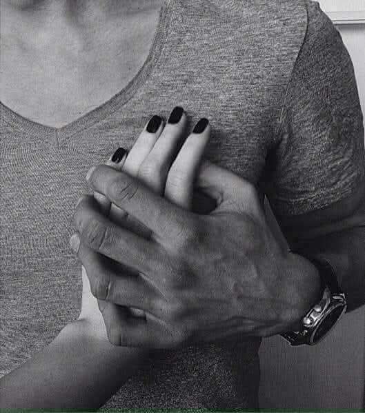 Black and white optical illusion where clasped hands appear to form a face with dark nail polish as eyes