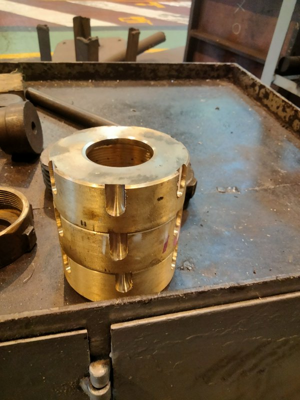 Slotted machined brass bushing sits on a worn metal workshop work tray in a machine shop
