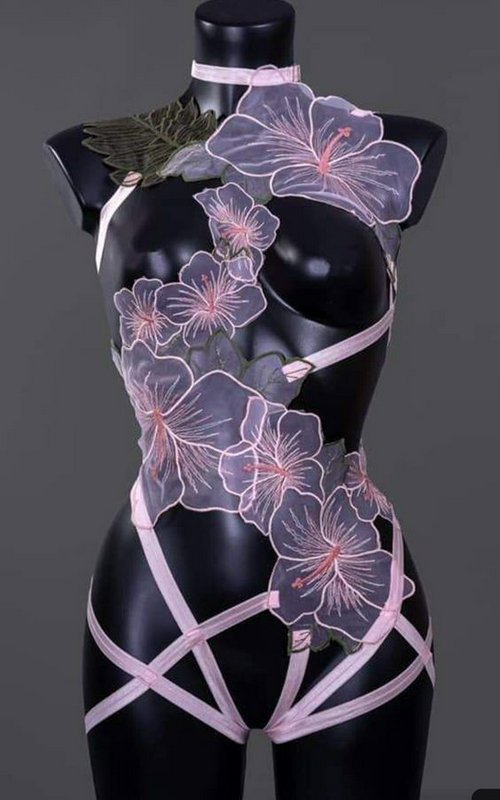 Sheer floral embroidered strappy lingerie displayed on a black torso mannequin against a plain gr...