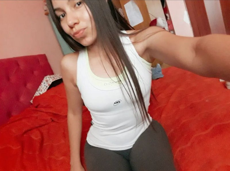 Young woman with long straight dark hair takes a casual selfie while sitting on a red bed