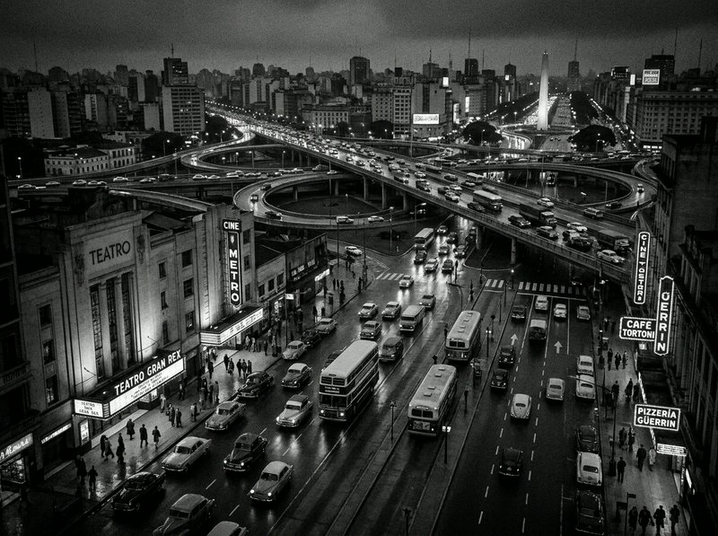 Black-and-white city scene with a multi-level highway and busy traffic near a historic theatre district.