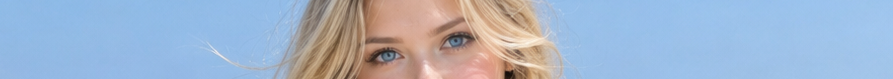 Close-up of a woman's bright blue eyes and windblown blonde hair against a clear blue sky