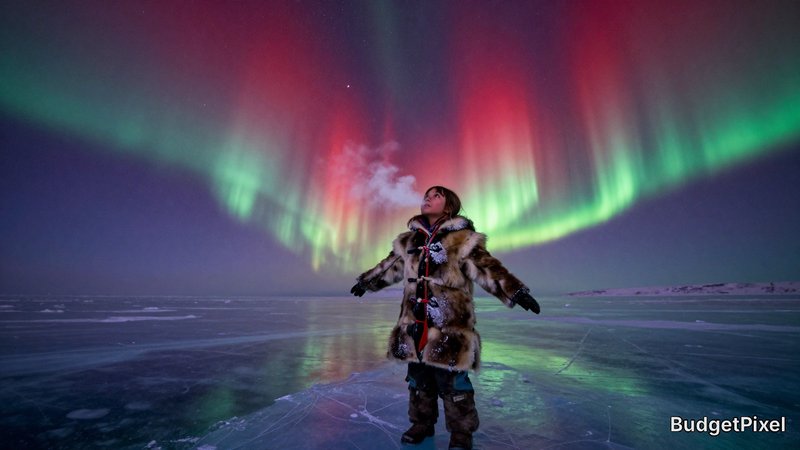 Child in a fur coat standing on a frozen lake under vibrant aurora borealis lights.