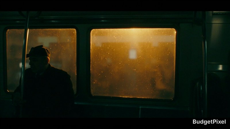 Silhouette of a person seated inside a dim bus at night, warm orange light through rain-speckled windows.