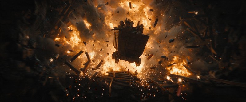 Mining cart carrying passengers flies mid-air surrounded by a massive fiery explosion and flying ...