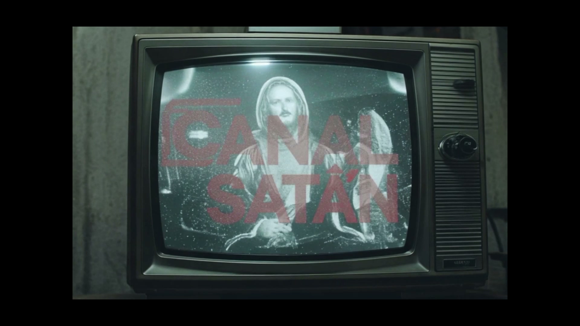 Vintage CRT television displaying grainy monochrome footage overlaid with bold red Canal Satan ti...