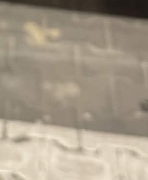 Blurry gray pavement with white patches resembling snow and faint markings.