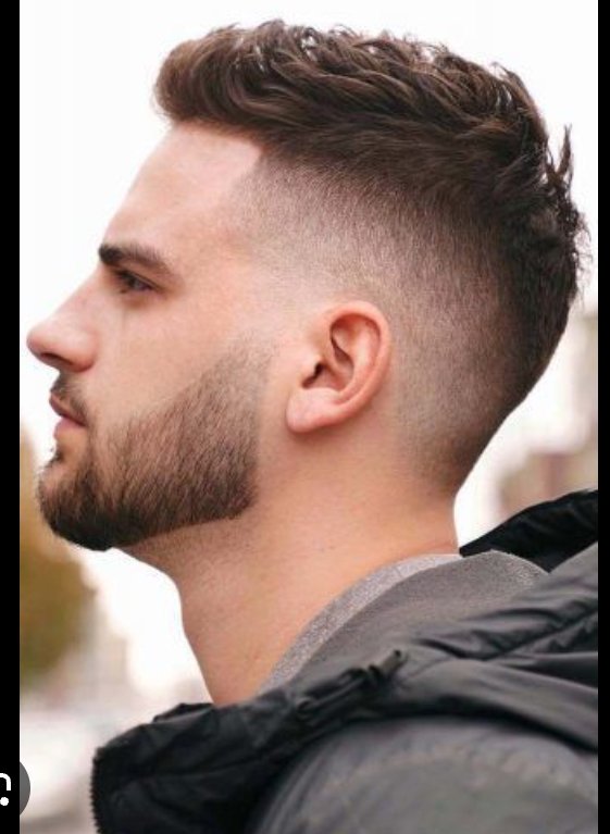 Side profile view of a man with a curly textured high fade haircut and neatly trimmed short beard
