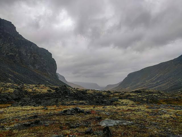 Overcast rocky arctic mountain valley flanked by steep craggy cliffs under heavy grey storm clouds