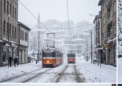 Two vintage orange trams travel along snow covered city street tracks during heavy falling snow