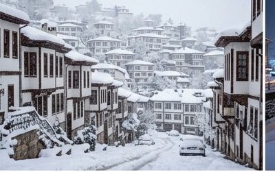 Heavily snow-covered hillside town lined with traditional timber-framed homes during a steady win...