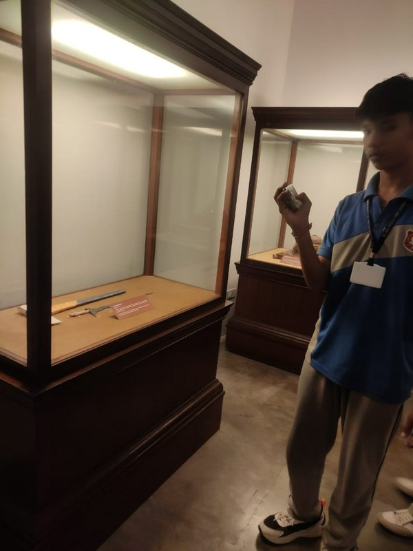 Teen student with lanyard ID takes photos of historical artifacts in wood and glass museum displa...