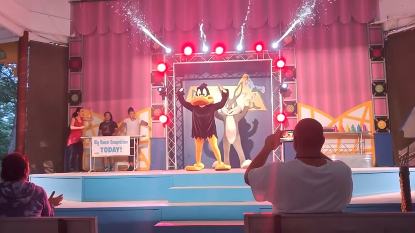 Costumed Daffy Duck celebrates on a vibrant theme park stage during a live family show