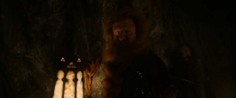 Bearded dwarf holds a glowing lantern while exploring a dark rocky cave with a companion behind him.