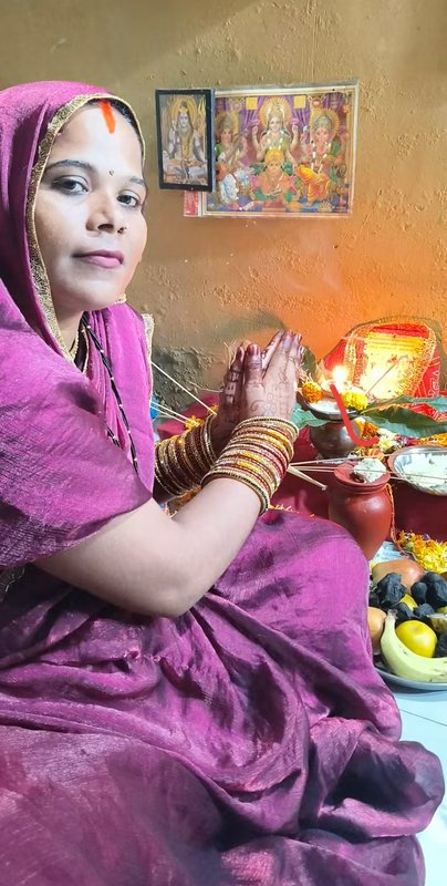 Woman in magenta sari sits in prayer pose performing a traditional Hindu home puja ceremony