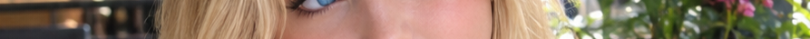 Extreme panoramic closeup of a bright blue eye framed by blonde hair beside pink flowering green foliage