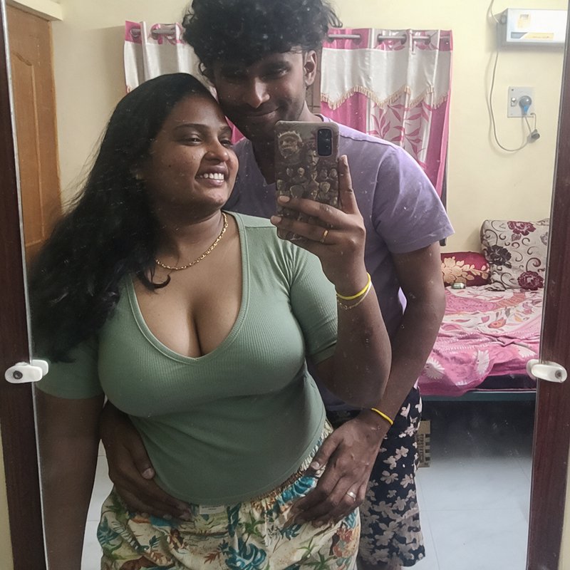 Smiling young South Asian couple taking a casual mirror selfie together in their home bedroom