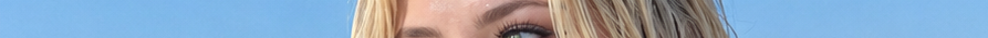 Cropped closeup of a blonde woman's eye and forehead against a bright clear blue sky