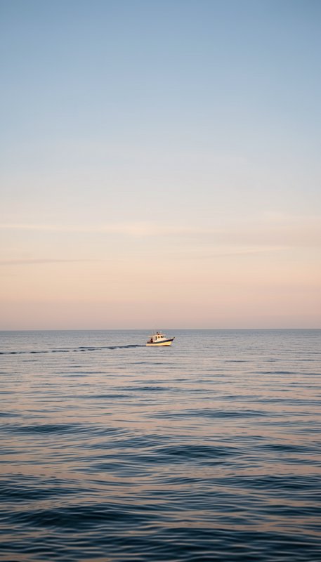Small fishing boat crosses calm rippled ocean beneath a soft pastel sunset sky