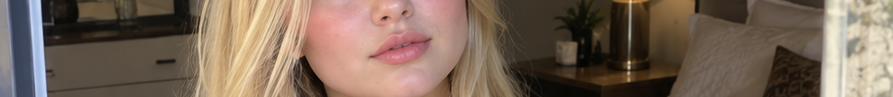 Cropped closeup of a blonde woman's lower face with soft natural makeup in a cozy bedroom