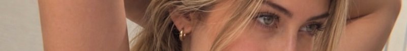 Close-up of a blonde woman's eyes and gold hoop earring, arms raised beside her head