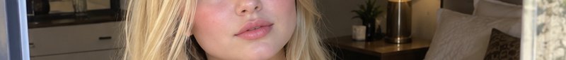 Cropped closeup of a blonde woman's lower face with soft natural makeup in a cozy bedroom