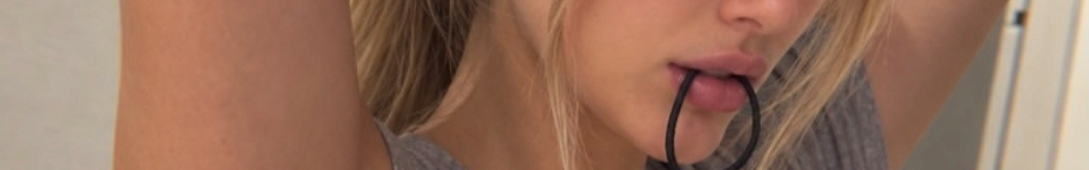 Close up of a blonde woman holding a black hair tie between her lips while styling her hair