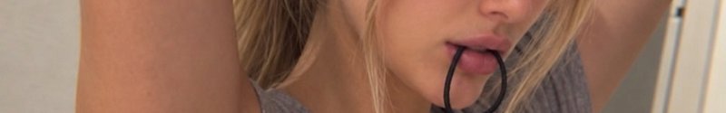 Close up of a blonde woman holding a black hair tie between her lips while styling her hair