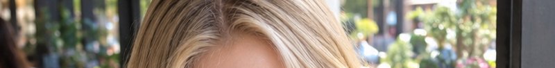 Close up of highlighted blonde hair crown with a sunlit blurred outdoor street background