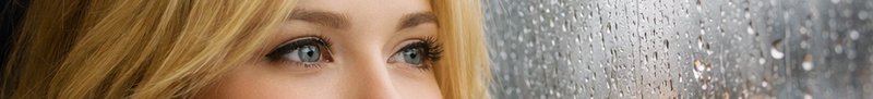 Close-up of a blonde woman's light blue eyes next to a rain-streaked window pane